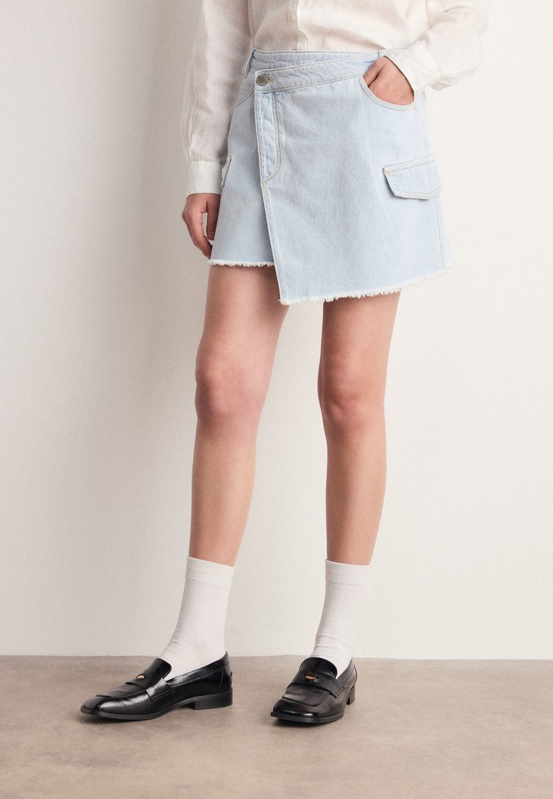 Hele hall denim seelik purunenud äärise, küljetasku ja rätsepäe disainiga. Kombineeritud mustade loafers'idega ja valgete põlvikutega.