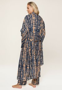 Dlhý kimono s otvoreným predným dielom v námorníckej modrej farbe s abstraktným oranžovým vzorom. Obsahuje široké rukávy a zodpovedajúci opasok. Mäkko tkanina s splývavým dizajnom.