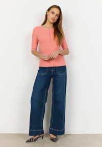 Light coral ribbed top with three-quarter sleeves and button detail, paired with wide-leg dark denim jeans and black and white striped heels.