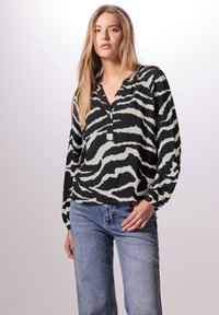 Blouse noire et gris clair avec un motif zèbre, dotée d'un décolleté en V et de manches longues, associée à un jean bleu clair.