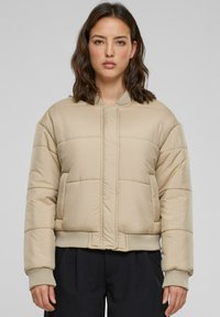 Beige puffjacka med en kortad design, ribbade ärmslut och en dragkedjelös front. Har stickade horisontella paneler för textur och värme.