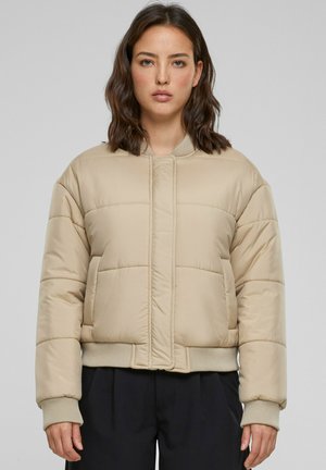 Beige fôretjakke med en kort design, ribbede mansjetter og glideløs front. Har sydd horisontale paneler for tekstur og varme.