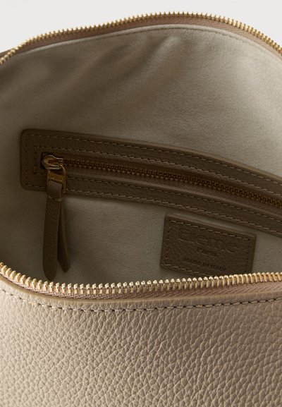 Κοντινό πλάνο στο εσωτερικό μιας μπεζ δερμάτινης τσάντας που δείχνει μια τσέπη με φερμουάρ με δερμάτινη λαβή και ραμμένη ετικέτα με το όνομα της μάρκας που γράφει "Elleme Paris Made in Italy".