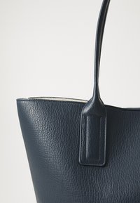Sac fourre-tout en cuir bleu marine avec une finition texturée, présentant un design structuré et des poignées fines. Le dessus ouvert met en valeur un intérieur contrasté.