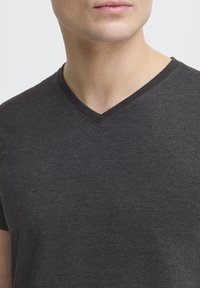 Camiseta de cuello en V gris oscuro con una textura suave, mangas cortas y un cuello con contraste sutil. Diseño simple y clásico.