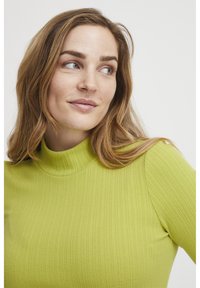 Ribbad polotröja i lysande limegrön, med en figurnära design och subtil textur. Kragen är hög och sömlös.