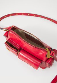 Rote Leder-Crossbody-Tasche mit einem Hauptfach mit Reißverschluss, zwei Fronttaschen, goldfarbenen Beschlägen und einem strukturierten Tragegurt.