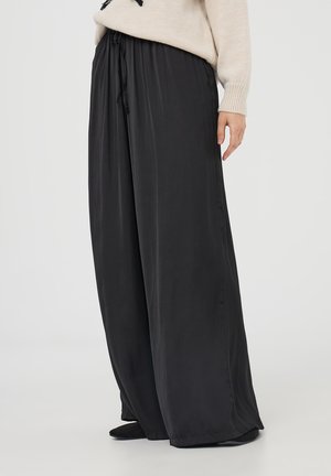 Pantaloni neri a gamba larga realizzati in tessuto morbido, con vita regolabile e design fluttuante, caratterizzati da una texture liscia e una lunghezza completa.