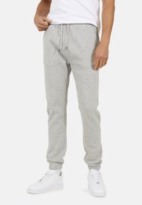Man in lichtgrijze sweatpants met een trekkoord in de taille en elastische boorden, gecombineerd met witte sneakers en een wit T-shirt.