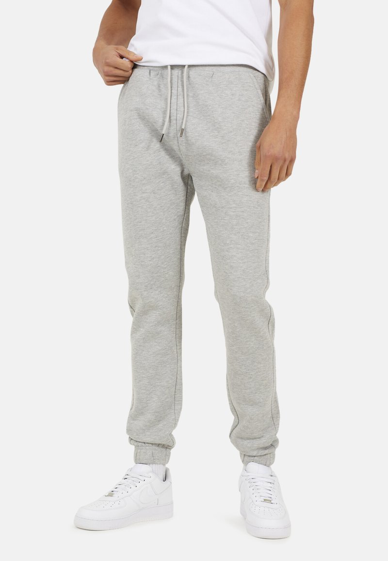 Man in lichtgrijze sweatpants met een trekkoord in de taille en elastische boorden, gecombineerd met witte sneakers en een wit T-shirt.