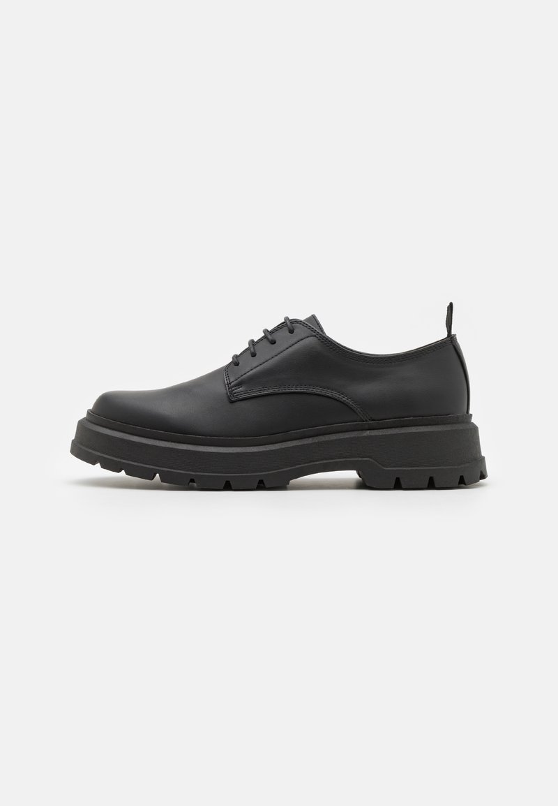 Chaussure basse à lacets en cuir noir avec semelle épaisse et robuste et boucle au talon, présentée sur fond blanc.
