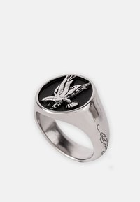 Anillo de plata con una piedra ovalada negra y un diseño de águila grabado. La banda tiene un acabado liso con detalles grabados en el lateral.