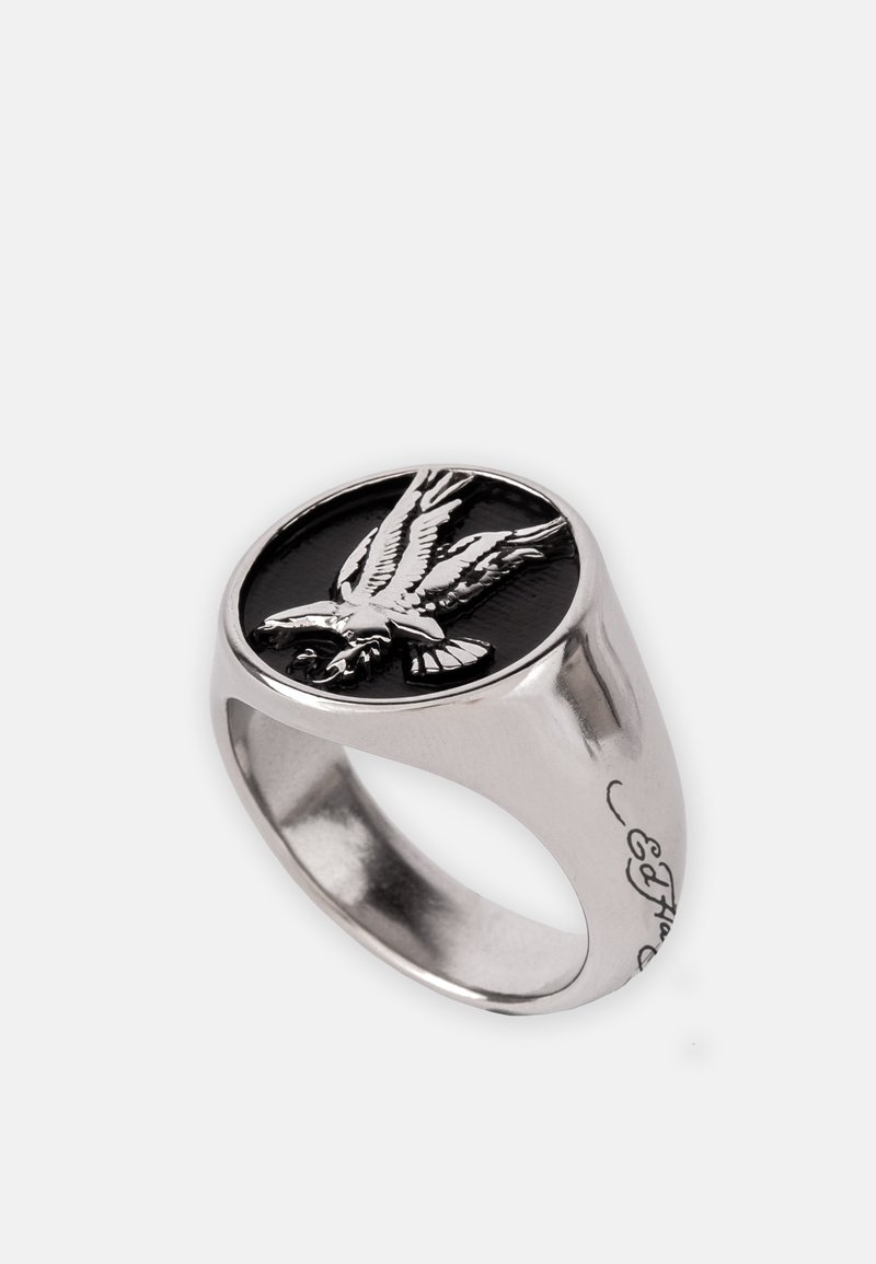 Anillo de plata con una piedra ovalada negra y un diseño de águila grabado. La banda tiene un acabado liso con detalles grabados en el lateral.