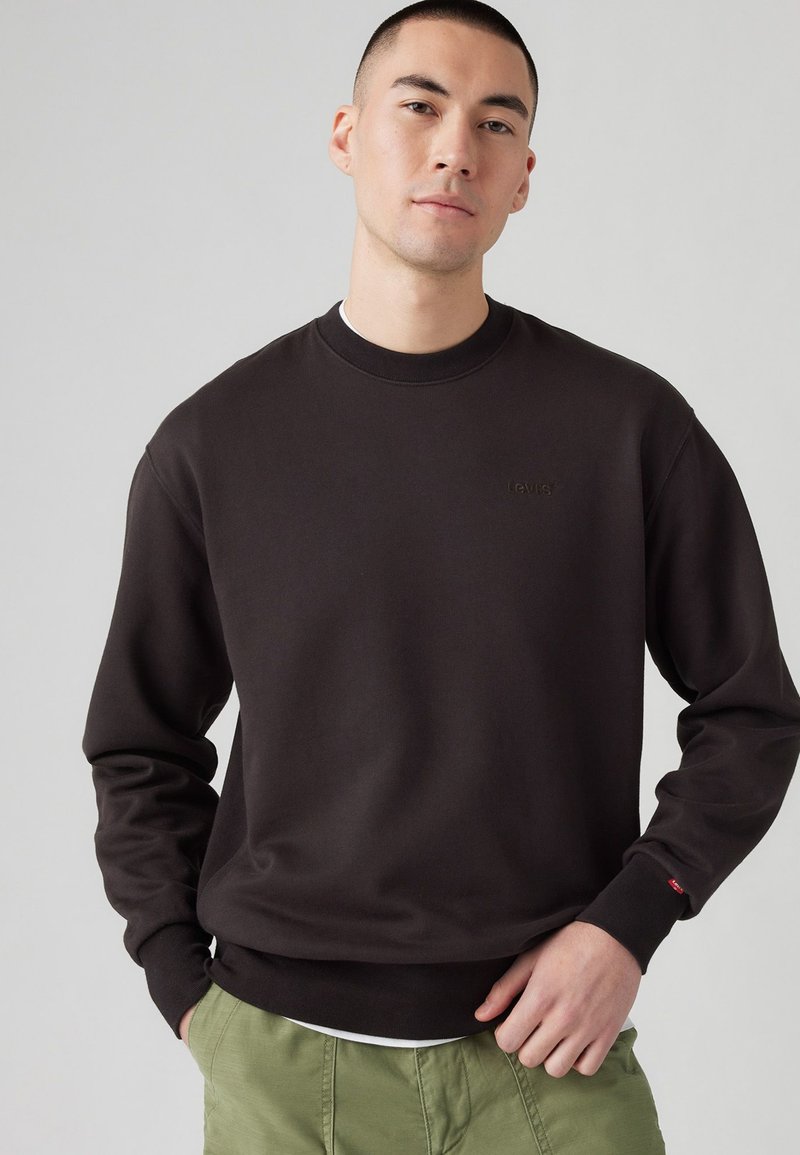 Sudadera de color marrón oscuro con cuello redondo, mangas largas y puños de canalé. Presenta el sutil logo "Levi's" en el mismo color. Tejido texturizado.
