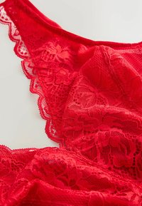 Rote Spitzenunterwäsche mit floralen Mustern und gewellten Kanten, die eine glatte Textur und feine Designdetails zeigt.