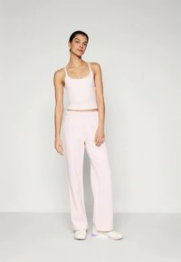 Light pink tank top and matching wide-leg pants made from soft fabric, featuring a simple design. Model stands wearing white sneakers.