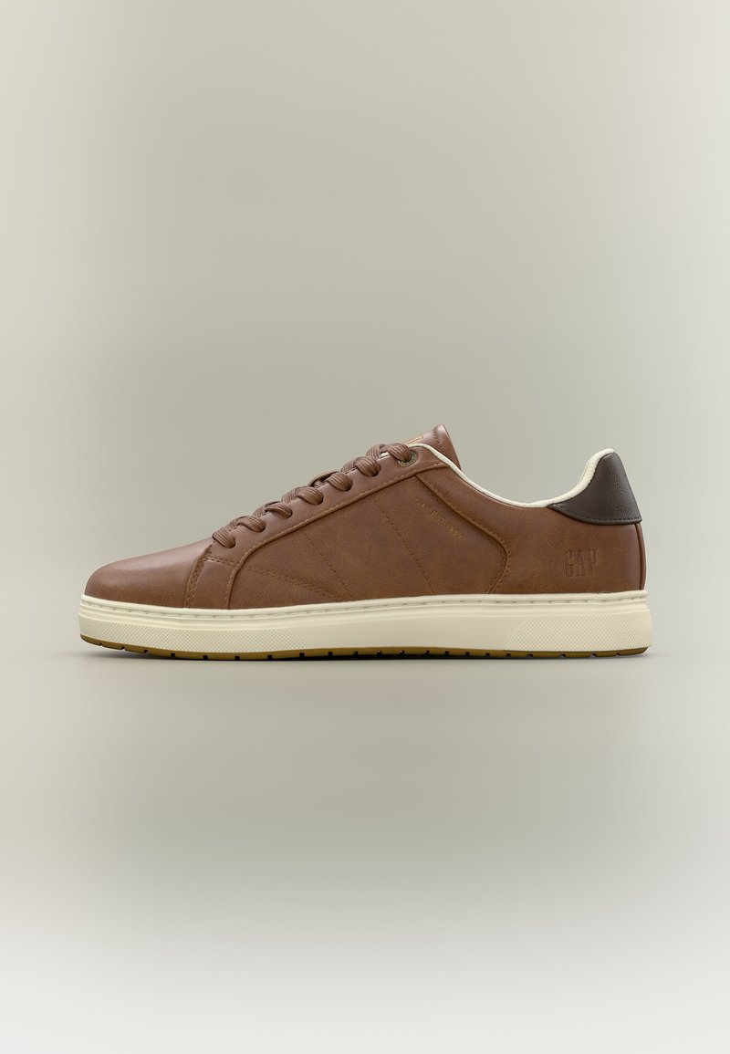 Baskets basses en cuir marron avec semelle en caoutchouc crème et patch talon marron foncé, design à lacets sur le côté, sur fond neutre.