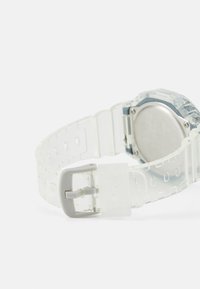 Montre en plastique transparent avec un bracelet transparent, des accents argentés et un boîtier rond. Dispose d'une fermeture à boucle sécurisée.