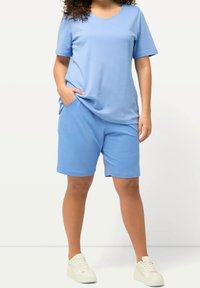 Ljust blå bomullströja med korta ärmar och V-ringning, tillsammans med matchande shorts. Vita sneakers fulländar outfiten.