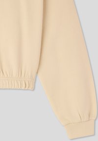 Top beige a maniche lunghe con polsini e cintura elasticizzati. Tessuto liscio e non testurizzato con una vestibilità morbida. Design minimalista.