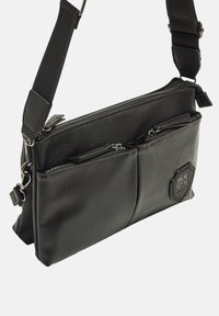 Borsa a tracolla nera in pelle con due tasche con zip, superficie testurizzata, tracolla regolabile e dettaglio del logo esagonale.