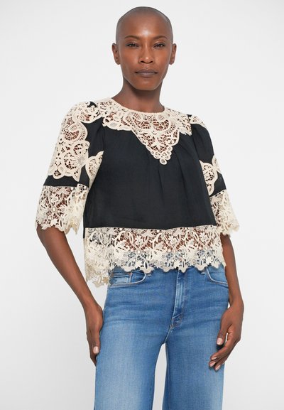 Blusa nera corta con dettagli in pizzo beige intricati intorno al colletto e alle maniche, con un bordo in pizzo a scallopato nella parte inferiore.