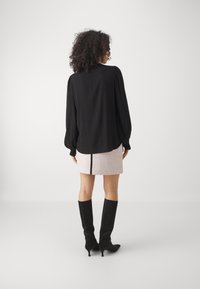 Chemisier noir à manches longues avec des épaules bouffantes, associé à une mini-jupe rose à motifs et des bottes noires ajustées jusqu'aux genoux.