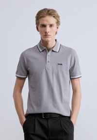 Γκρι πόλο μπλούζα με μαύρο και λευκό ριγέ γιακά, τρία κουμπιά στο κολάρο και κεντημένο λογότυπο στο αριστερό στήθος. Υφασμάτινο μείγμα βαμβακιού, λείο στην αίσθηση.