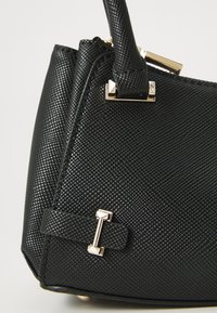Black handbag with a textured surface, gold hardware accents, and a structured shape. Features a prominent strap and a decorative buckle detail.