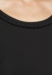 Svart linne med en bred, rund halsringning och flätad textur längs kanten, tillverkat av ett smidigt, elastiskt tyg.