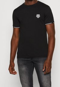 Camiseta de algodón negra con cuello redondo, mangas cortas con acentos en blanco y un gráfico de tigre en el lado izquierdo del pecho.