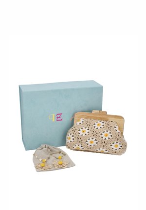 Un bolso de mano beige de ganchillo con margaritas blancas y amarillas, pendientes de flores a juego y una caja de regalo azul sobre un fondo blanco.