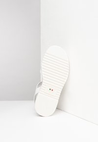 Sandalo bianco con una suola testurizzata caratterizzata da scanalature orizzontali. La parte superiore morbida include un design a cinghia per un indossamento confortevole.
