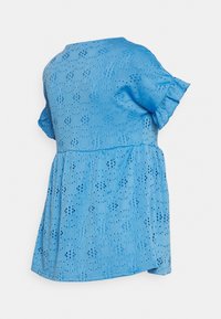 Top azul claro de manga curta com textura de ilhós e detalhes em babados. Barra ligeiramente evasê. Tecido macio e respirável com padrões decorativos recortados.