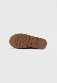 Brun gummisål med en zigzag-mønster, der har en glat tekstur og afrundede kanter. Designet er holdbart og funktionelt.