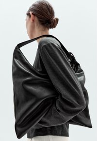 Schwarze Lederhandtasche mit einem lässigen Design, großer Größe und einem einzigen Schulterriemen. Die Oberfläche wirkt glatt und hat eine weiche Textur.