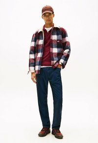 Rdeča in mornarsko modra karirana flis jakna z belim Sherpa ovratnikom, maroon polo majica spodaj, mornarsko modre hlače in črno-rdeči superge.