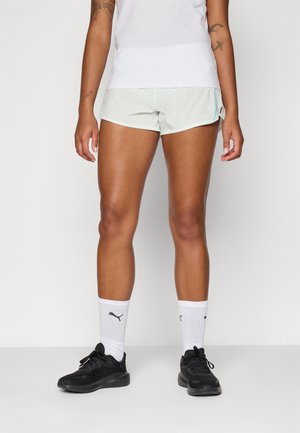 Lys grønne treningsshorts med en glatt tekstur, med sideslitser. Kombinert med svarte treningssko og hvite stripete sokker.