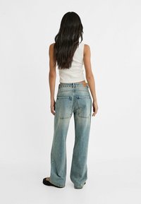 Jeans de pierna ancha de color azul claro con un acabado deslavado, dos bolsillos traseros y una etiqueta de cuero en la cinturilla. Combinados con una blusa blanca sin mangas.