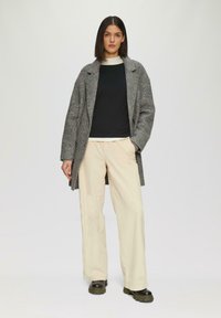 Grijs wollen blend jas met overmaatse revers, zwart langemouwen top, crèmekleurige wijde broek en zwarte chunky-soled laarzen.