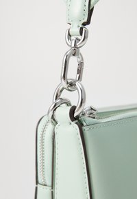 Borsa in pelle verde menta con chiusura metallica argentata, caratterizzata da una texture liscia, cuciture precise e un dettaglio con cerniera lungo un bordo.