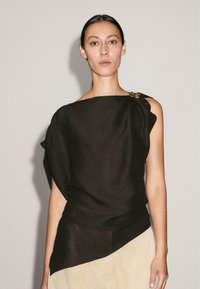 Top en lin noir avec un décolleté asymétrique et une coupe drapée, présentant un accent doré à l'épaule. Texture lisse avec une silhouette décontractée.