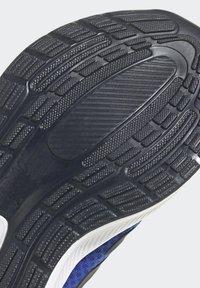 Suola di scarpa nera in gomma con motivi di battistrada testurizzati e scanalature, con un'area centrale liscia e un accento di intersuola bianca.