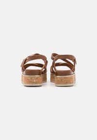 Sandali in pelle marrone con suola in sughero. Caratterizzati da fasce incrociate e dettaglio con fibbia; texture liscia con una finitura naturale.