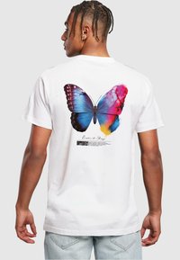 Hvid bomulds T-shirt med et farverigt sommerfugl grafik på ryggen, med blå, pink og gule accenter, samt tekst under designet.