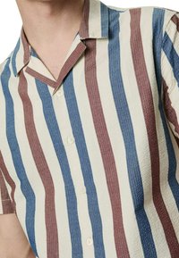 Camicia a maniche corte con chiusura a bottoni, caratterizzata da strisce verticali in blu, rosso e crema. Tessuto testurizzato con colletto.