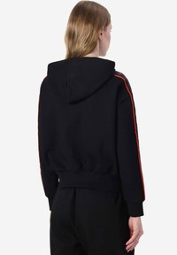 Felpa nera con una texture morbida, dotata di cappuccio, vita elasticizzata e strisce laterali rosse lungo le maniche. Design semplice e funzionale.