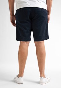Donkerblauwe katoenen shorts met een rechte snit, twee achterzakken en omgeslagen zomen, gedragen met witte sneakers met een logo.
