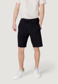 Black cotton shorts with an elastic waistband, drawstring, and side pockets, paired with white sneakers and a light-colored t-shirt.