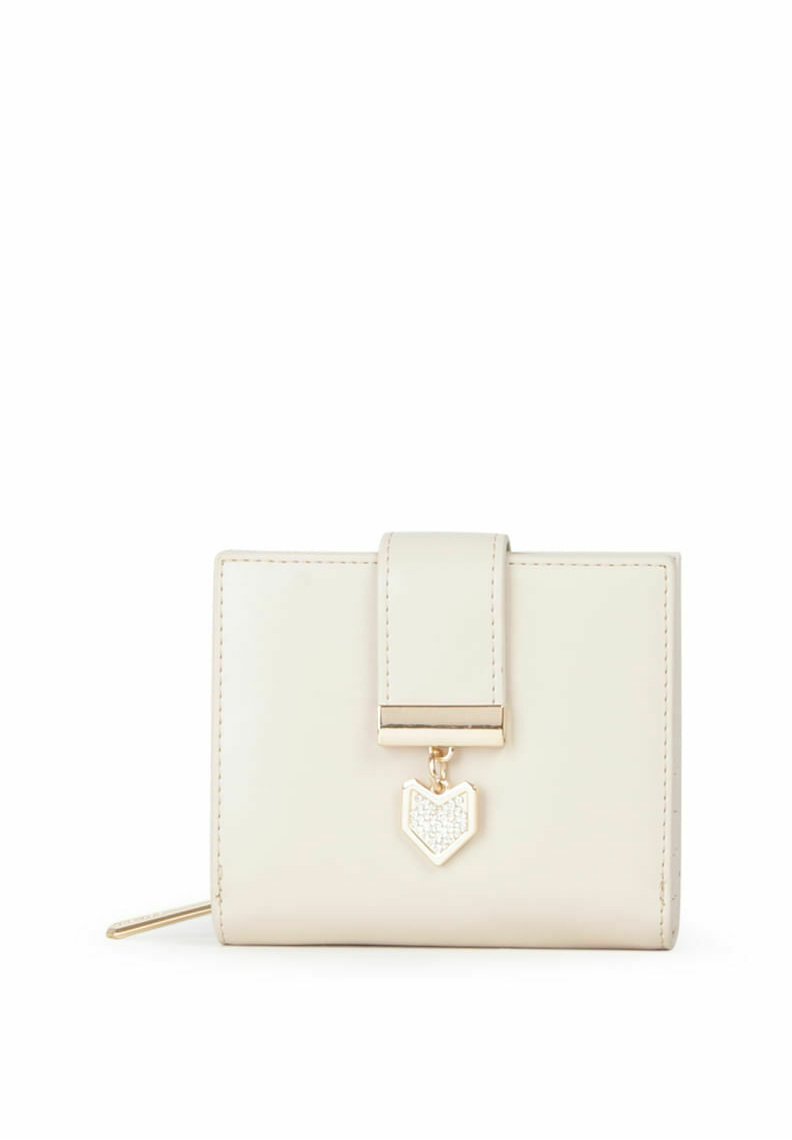 Cartera de cuero crema con herrajes dorados, cierre de solapa y un charm en forma de corazón con un detalle brillante. Forma cuadrada compacta.